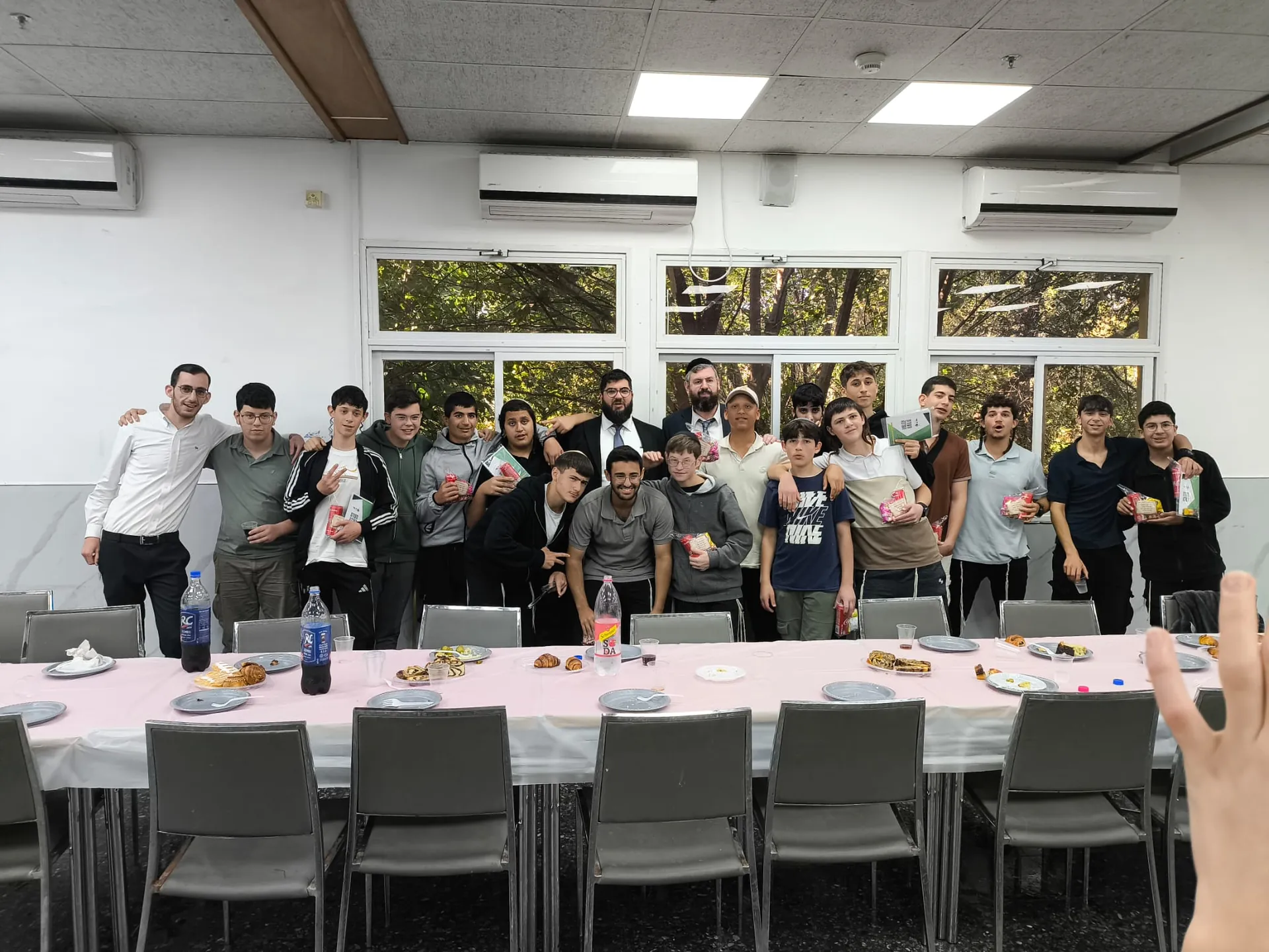 קבוצת תלמידים אחרת מצטלמת עם תעודות מול שולחן כיבוד - תעודות המחצית, ואחריהן מסיבה