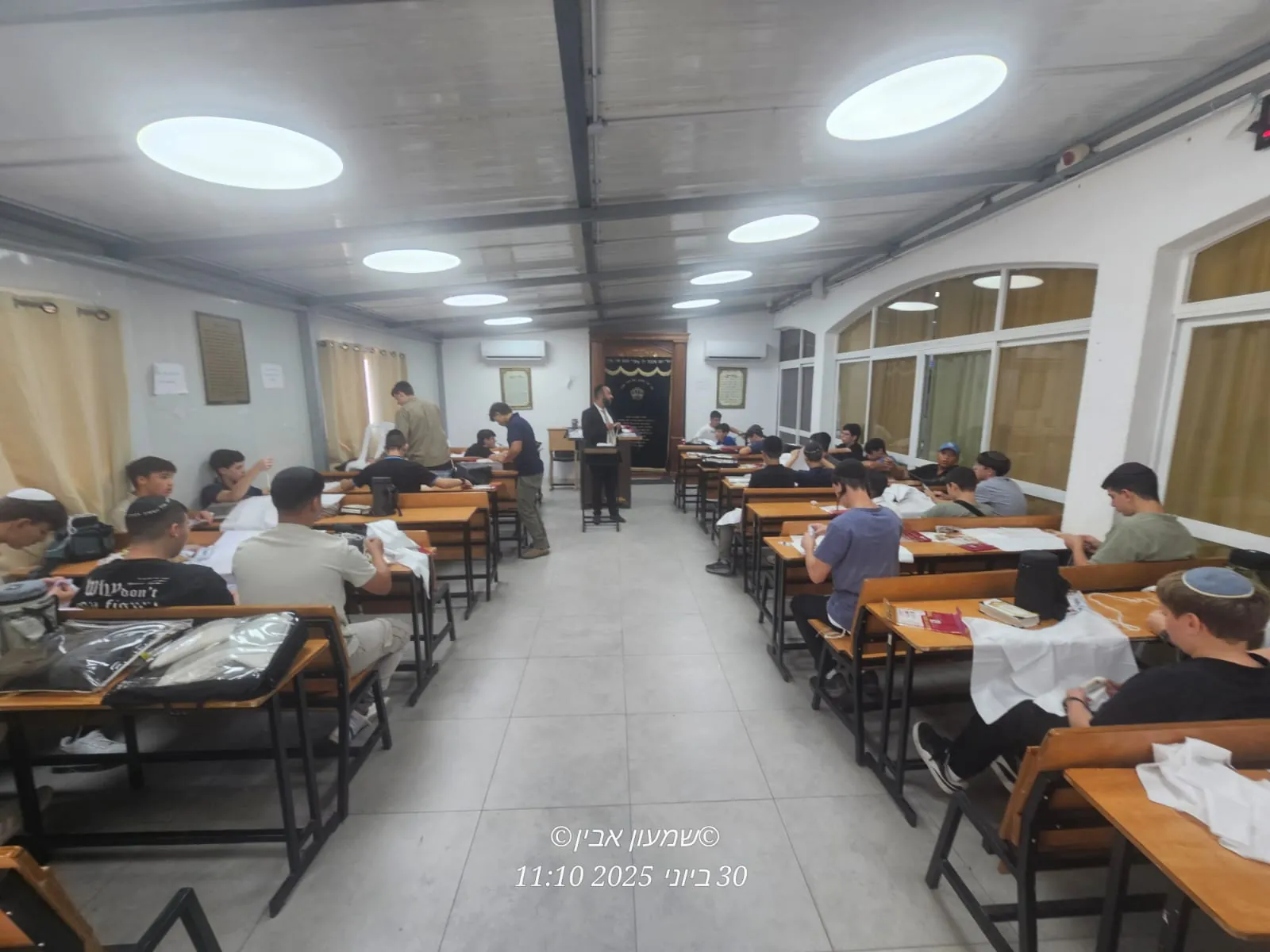 תלמידים עובדים בשולחנות בזמן הסבר רב - סדנת הכנת ציציות בבית המדרש