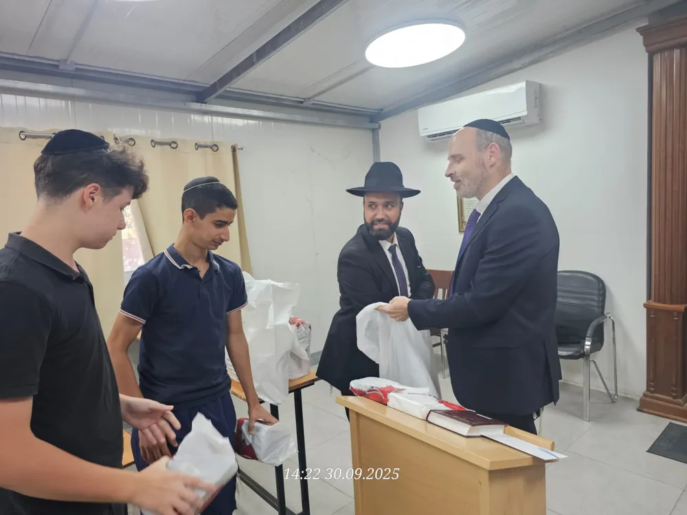 רבנים ותלמידים מחלקים חבילות ליד דוכן - ערב ראש השנה בקברי צדיקים