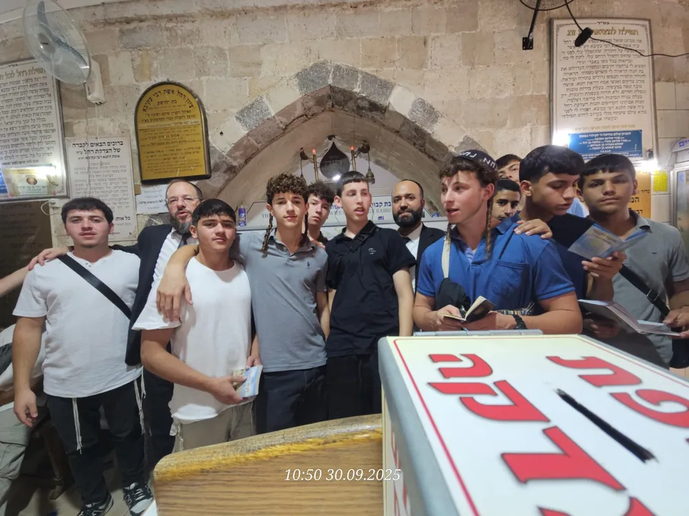 תלמידים ורבנים עומדים בציון קבר ומחזיקים ספרי תפילה - ערב ראש השנה בקברי צדיקים