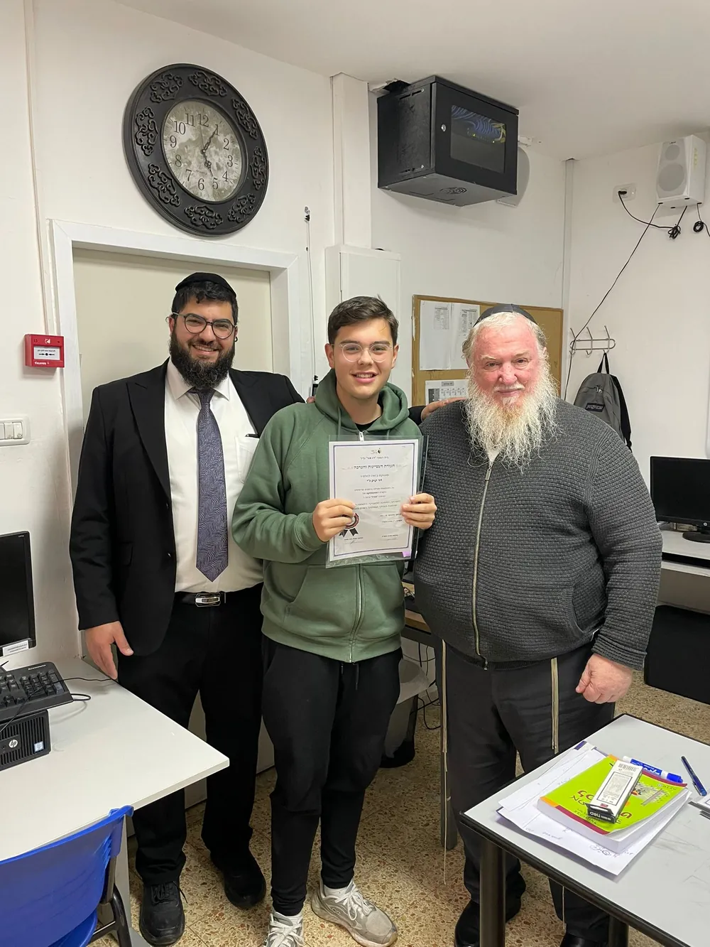 תלמיד עם תעודה לצד שני אנשי צוות - תעודות המחצית, ואחריהן מסיבה