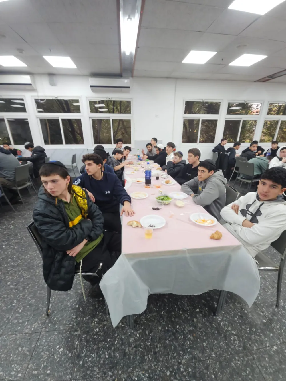 תלמידים יושבים לאורך שולחן סעודה ומביטים למצלמה - סיום מסכת - תעודה ביד וסעודה משותפת