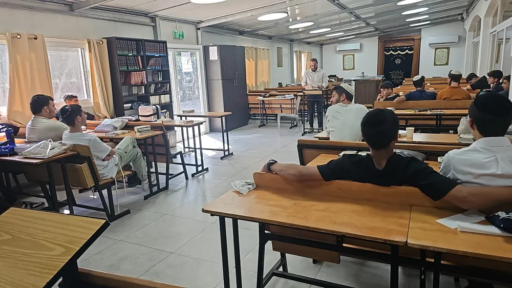 מרצה בחולצה לבנה עומד מול תלמידים בבית המדרש - בית מדרש מלא לקראת הימים הנוראים