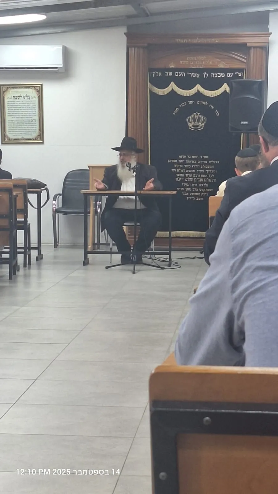 רב עם זקן וכובע מדבר במיקרופון בבית המדרש - בית מדרש מלא לקראת הימים הנוראים